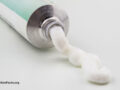 A white and turquoise cream tube with some cream spreading out