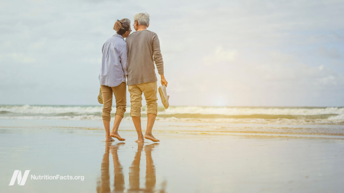 Senior couple walking on the beach holding hands and barefoot at sunrise