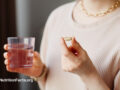 Person taking a supplement capsule with a cup of water